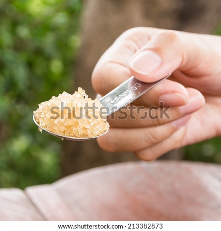 Hand holding a silver spoon heaped teaspoons of sugar.