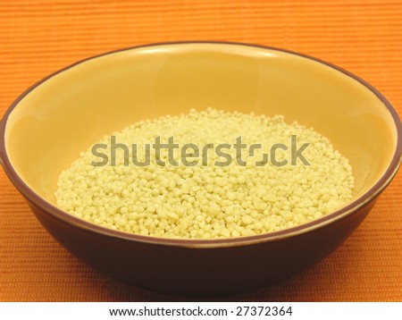 Yellow couscous in a orange bowl of ceramic on an orange background