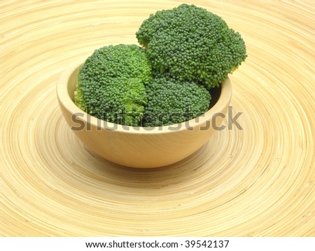Wooden bowl with broccoli on bamboo plate