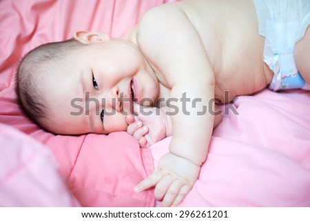 Asian baby girl crying and put her finger in her mouth. she lay on pink bed.