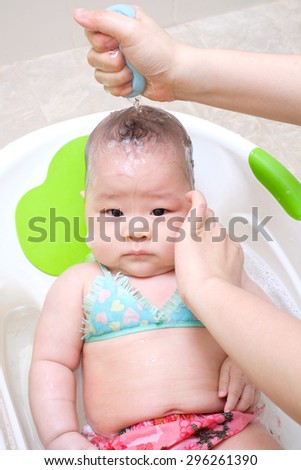 Mom washing her daughter hair. baby looking at the camera and not smile.