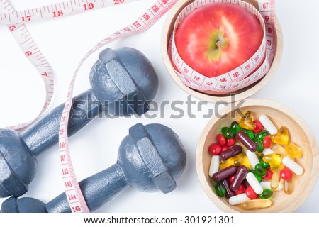 red apple and vitamin (medicine) in wooden bowl with waist measure and dumbbell  on white background