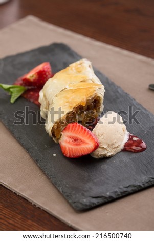Apple strudel cake served with strawberry and ice cream on the table at restaurant