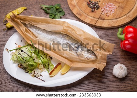 Grilled sea bass fish in paper with vegetables on wooden table