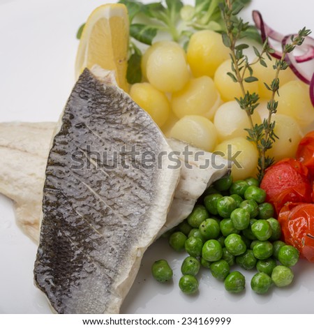 Grilled sea bass fish with potatoes, peas and tomatoes isolated on white background. Close up