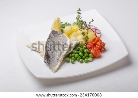 Grilled sea bass fish with potatoes, peas and tomatoes isolated on white background