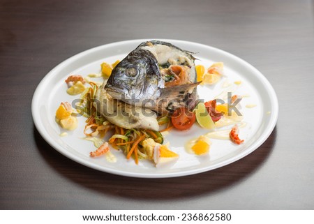 Grilled sea bass fish with vegetables and herbs isolated on wooden background