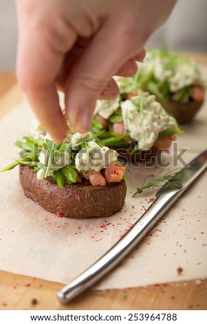 Chief's hand decorating sandwich with smoked salmon and rye bread on wooden table