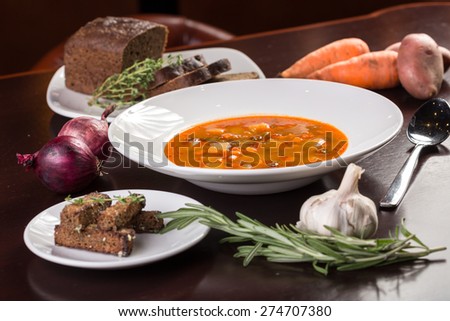Bowl of vegetable soup with ingredients on wooden table