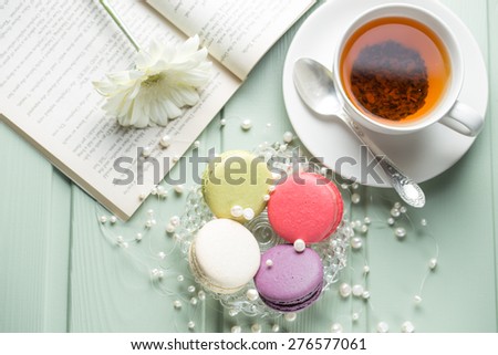 Vanilla, strawberry, pistachio and blueberry flavoured macaroons with pearls, flower and cup of tea on wooden background