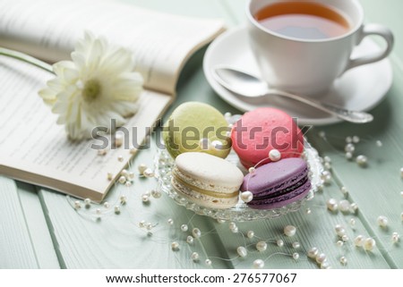 Vanilla, strawberry, pistachio and blueberry flavoured macaroons with pearls, flower and cup of tea on wooden background