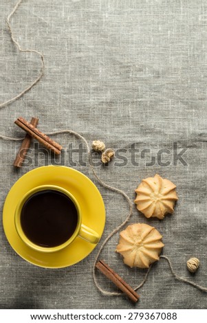 Black coffee in yellow cup with cookies and cinnamon sticks on grey fabric background