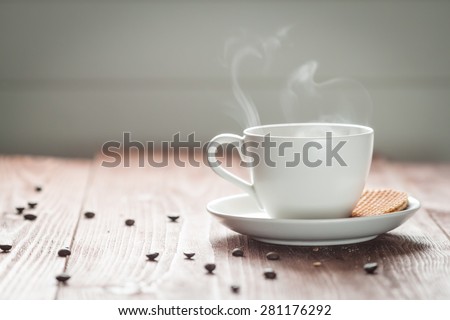 White cup of hot black coffee with steam and coffee beans on wooden table