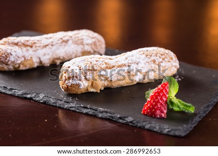 Creamy eclair dessert with strawberry on stone plate on wooden table