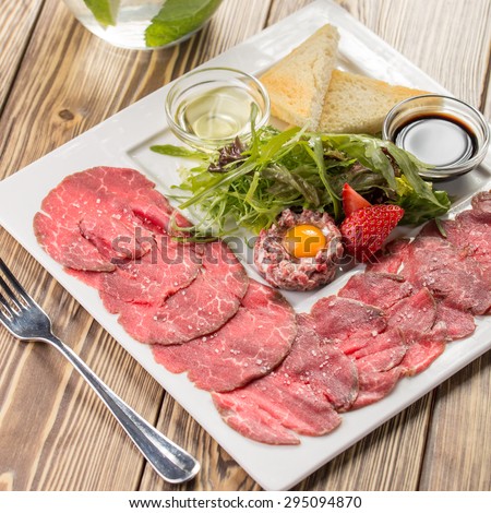 Steak tartar with cured meat and salad leaves on wooden background