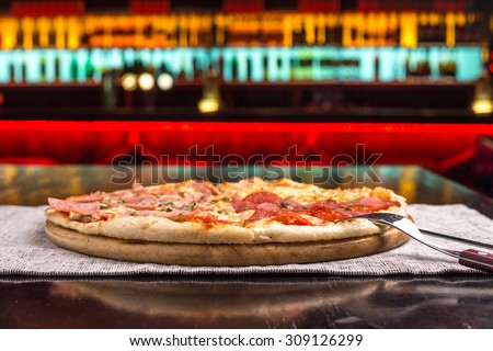 Different slices of pizza with bacon and salami on wooden board on table at the bar