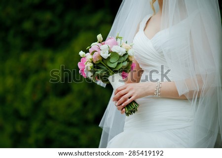 Close-up of roses wedding bouquet in a hands of a slim bride in a white wedding dress