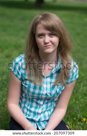 beautiful girl sitting on the grass with a sour face
