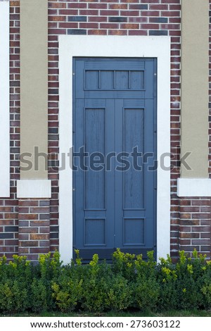 green bushes in front of entrance wooden door in an old brick wall