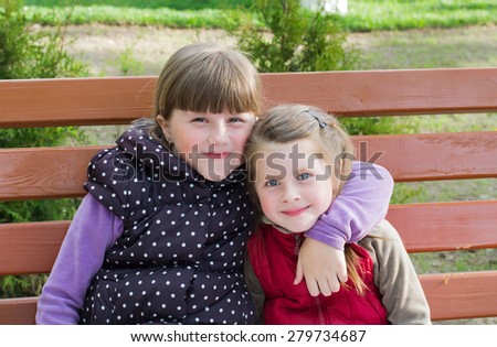 Two little funny girls cuddling sitting on a park bench