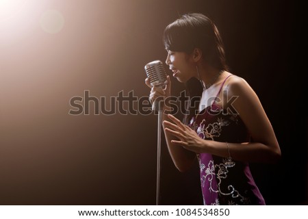 Asian woman singer holding a microphone singing.