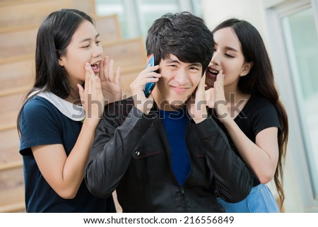 Female students asking a young Asian man to stop talking on his phone in the library.
