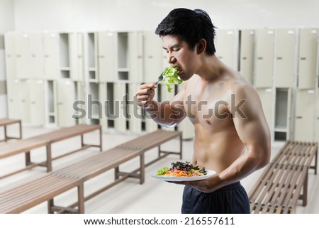 Fit Asian man losing weight by eating salad in gym.