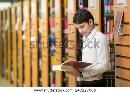 Asian student reads a book at the library. The bookshelf