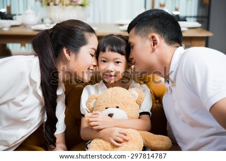 Parents kissing daughter with love in the house .Daughter hugging a teddy bear
