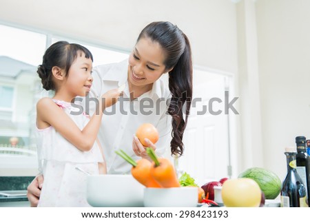 The daughter is entering her mother eating fruit. While cooking in the kitchen