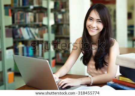 Asian student reading a book in the library. She used her computer to search for information