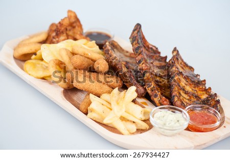 Grilled pork ribs with onion rings , fries, chips and three sauces
