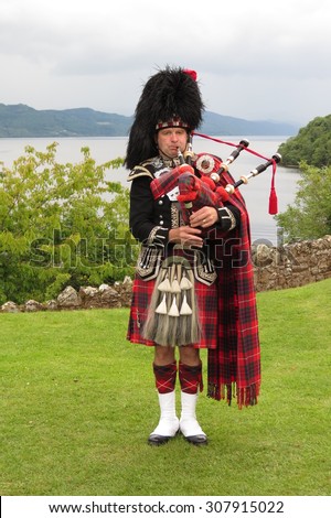 URQUHART CASTLE, SCOTLAND, UK - CIRCA AUGUST 2015: Scottish bagpiper dressed in traditional red and black tartan dress