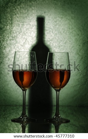 Two glasses of white wine and shadow of a bottle on a green background