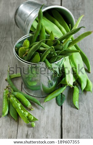Mix green beans and peas in small buckets on old wood table. Selective focus.