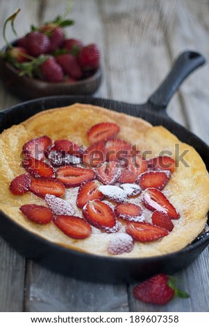 Big dutch baby pancake on pan with strawberry, dusted with powdered sugar. Selective focus.