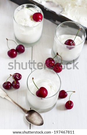 Homemade vanilla ice cream in frozen metallic container and glasses with ripe red cherry. Selective focus.