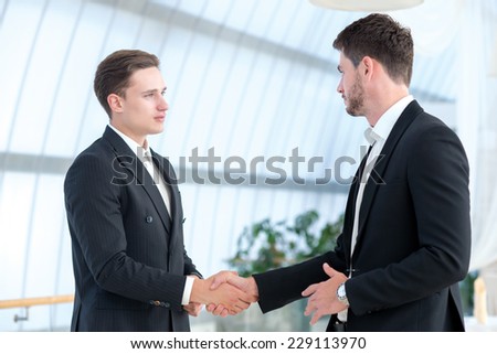 Good business deal. Two successful business partners are shaking hands and looking at each other with confidence