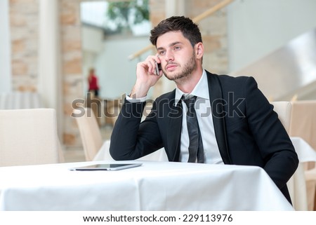 Doing job on the phone. Young and motivated businessman is sitting at the table and doing business by talking the mobile phone