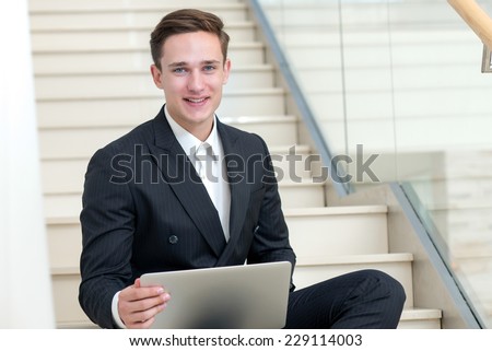 Good job. Handsome and successful businessman is sitting with laptop and smiling celebrating good business result