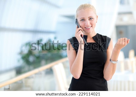 Well done deal on the mobile phone. Young and motivated businesswoman is standing and talking on the mobile phone looking directly into the camera