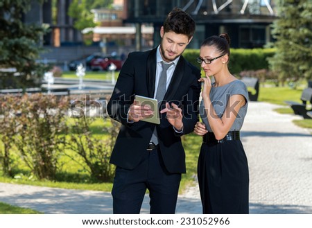 Teamwork. Pair of successful businessman are standing and watching in tablet. Businessman shows important stuff to her female business partner