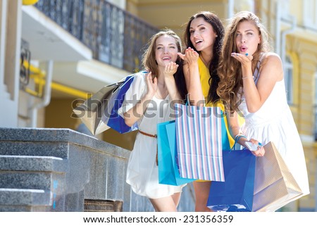 Best shopping wishes. Three young and pretty girls are standing with shopping bags. All are smiling and giving air kisses