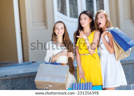 Great option in a shop. Three young and pretty girls are standing with shopping bags in front of the shop window and looking on a great sales offer