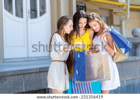 What is new in shopping. Three girlfriends are standing and looking is a shopping bag, while going shopping during weekend