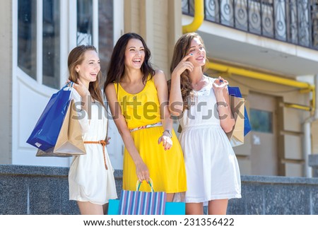 Shopping in a good mood. Three young and pretty girls are standing with shopping bags in a great mood. They are smiling and having fun