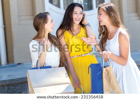 Shopping last news. Three young and pretty girls are talking to each other about best sales offers in shops and smiling. All are in a great mood
