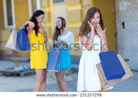 News about shopping sales on mobile phone. Young and pretty girl is talking on the sell phone and holding a shopping bags. Her friends girls are standing on the background with shopping bags.
