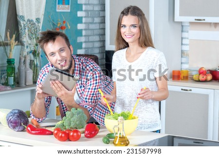 Looking for the ideal healthy recipe. Beautiful pair is standing on the kitchen and making tasty and healthy dinner. Young and handsome man is looking for the recipe in tablet and smiling