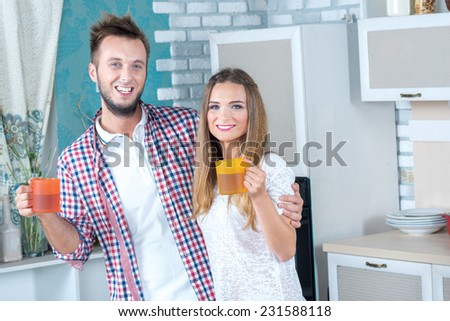 Drink for the ideal dinner. Beautiful pair is standing on the kitchen drinking something tasty from the cups and smiling before the great meal